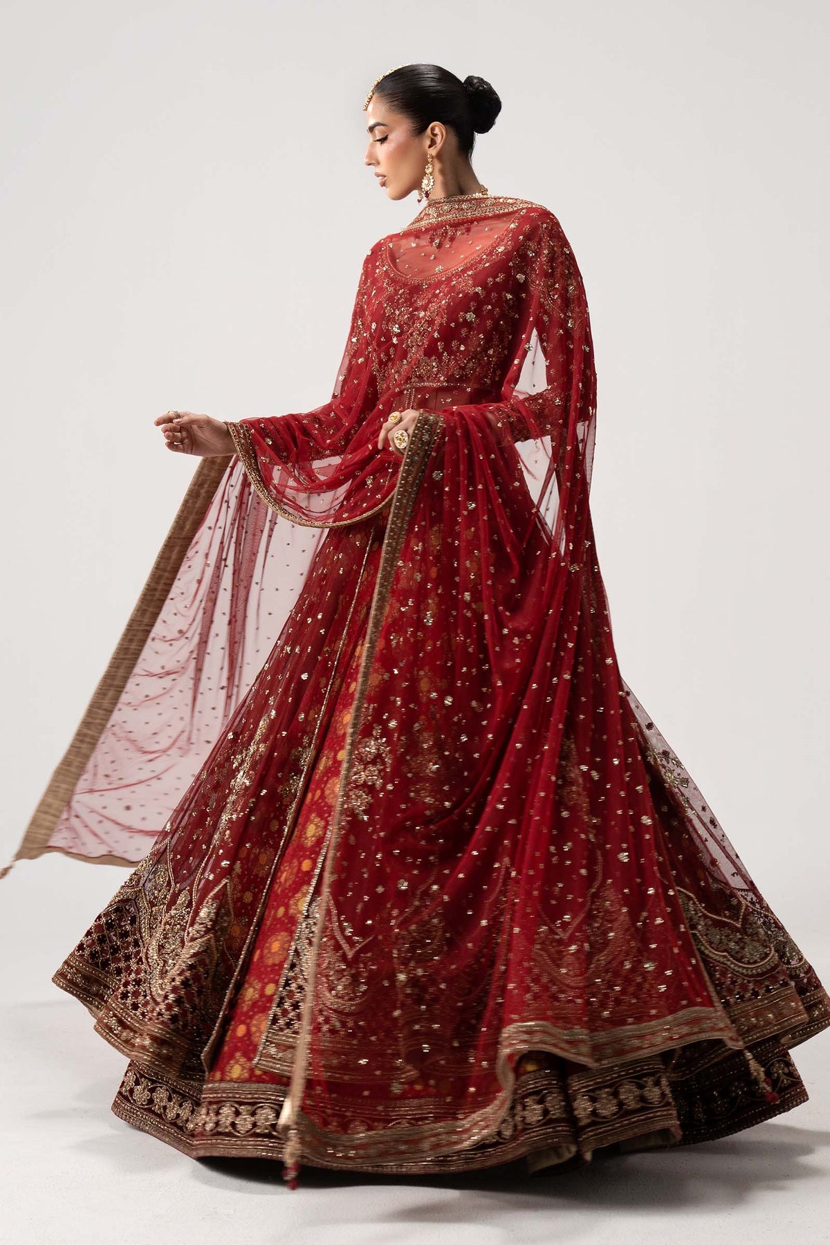 Back view of Maria B Bazif red embroidered bridal Pishwas with flowing net dupatta, elaborate gold hem border and full flare