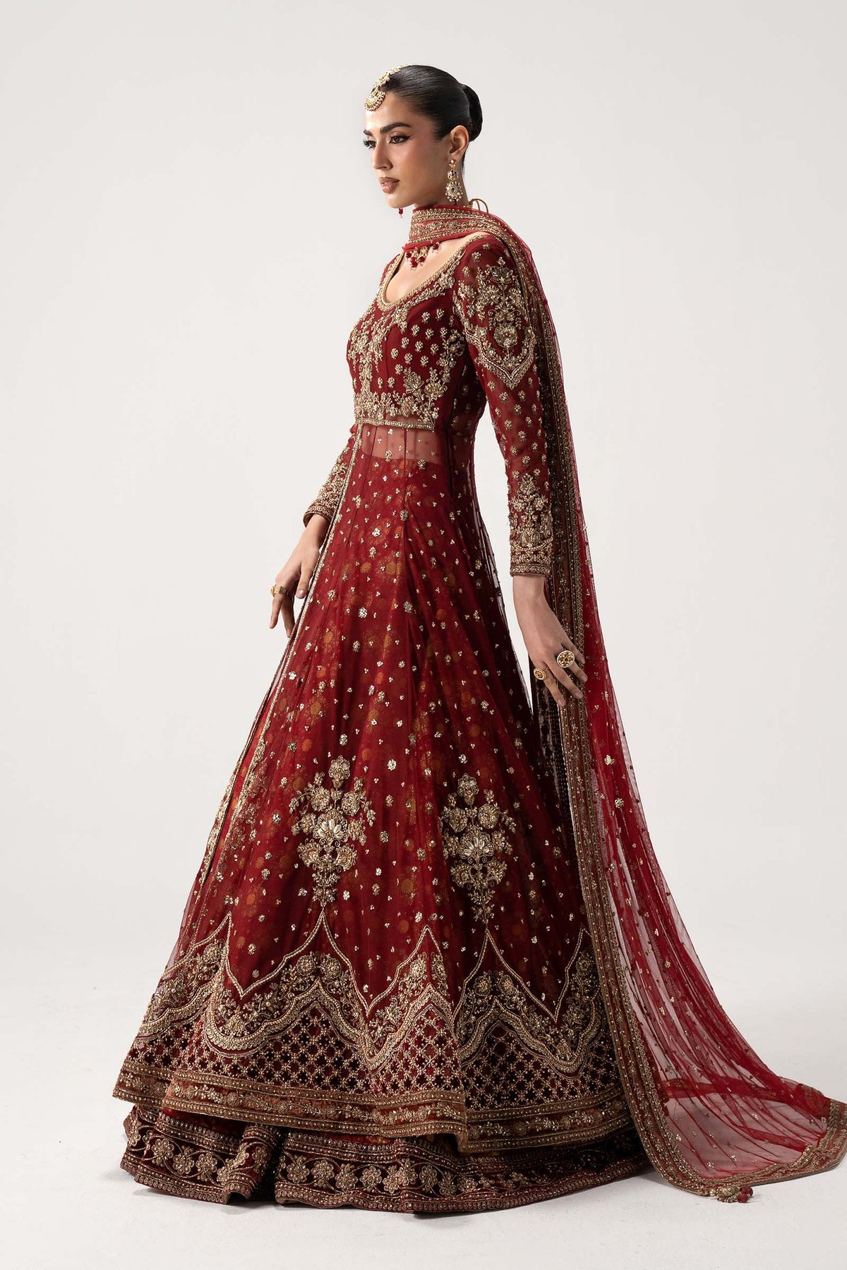 Side profile of Maria B Shadmani Retro Bazif wedding ensemble showcasing rich red net fabric and traditional gold embroidery